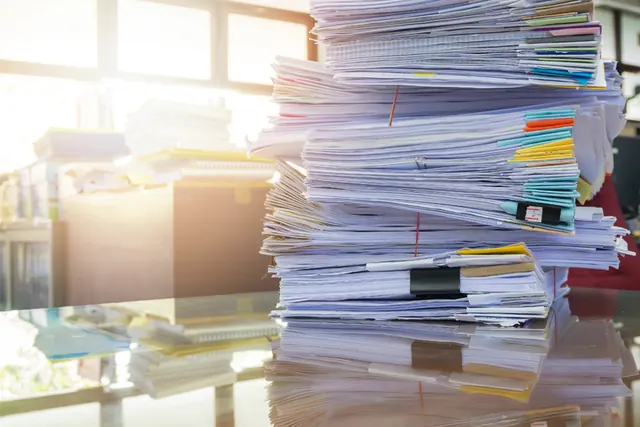 Hohe Stapel von Papierakten und Ordnern auf einem Bürotisch